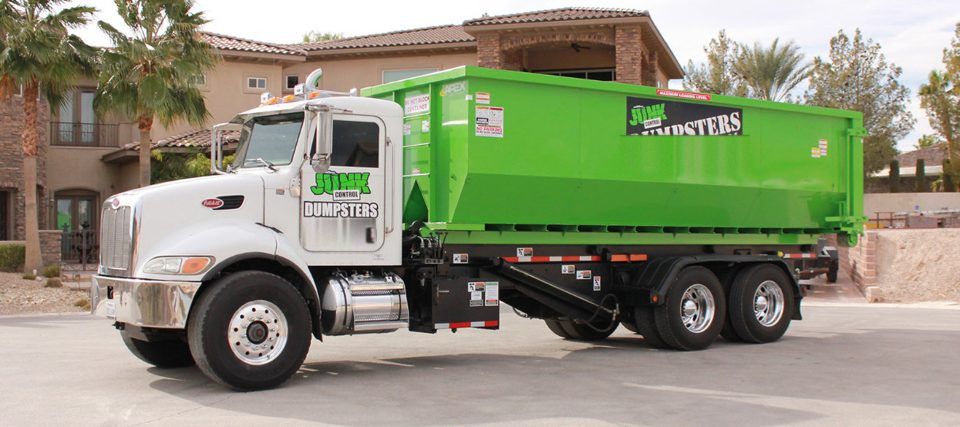 A Junk Control roll-off dumpster truck parked in front of a house